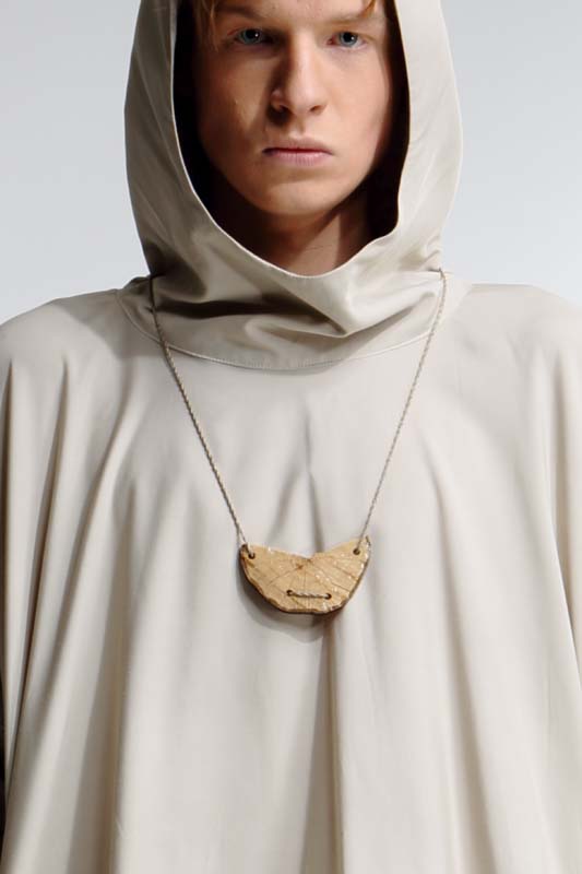 Model in a hooded sand coloured cape with a wooden pendant on a fine chain