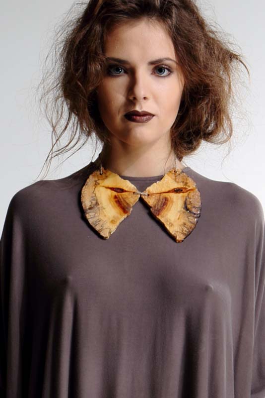 Model in a soft grey draped top wearing a carved wooden leaf collar