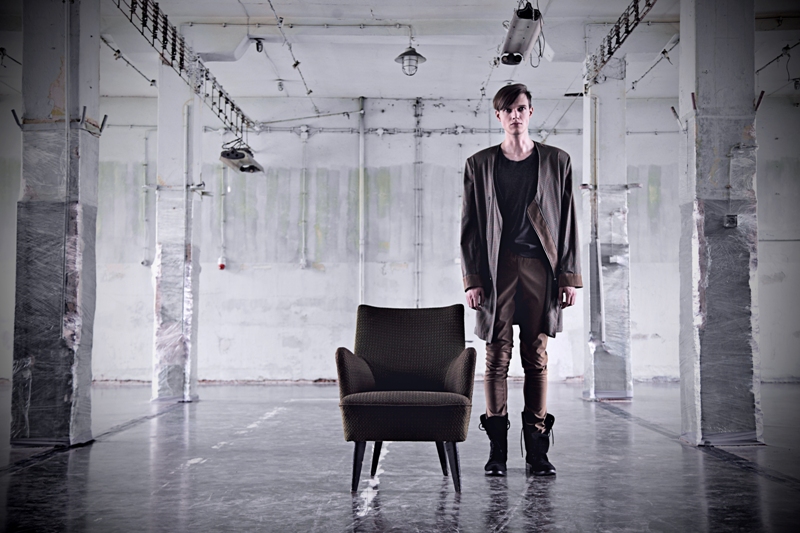 Model in a long charcoal coat and leather trousers in an empty hall